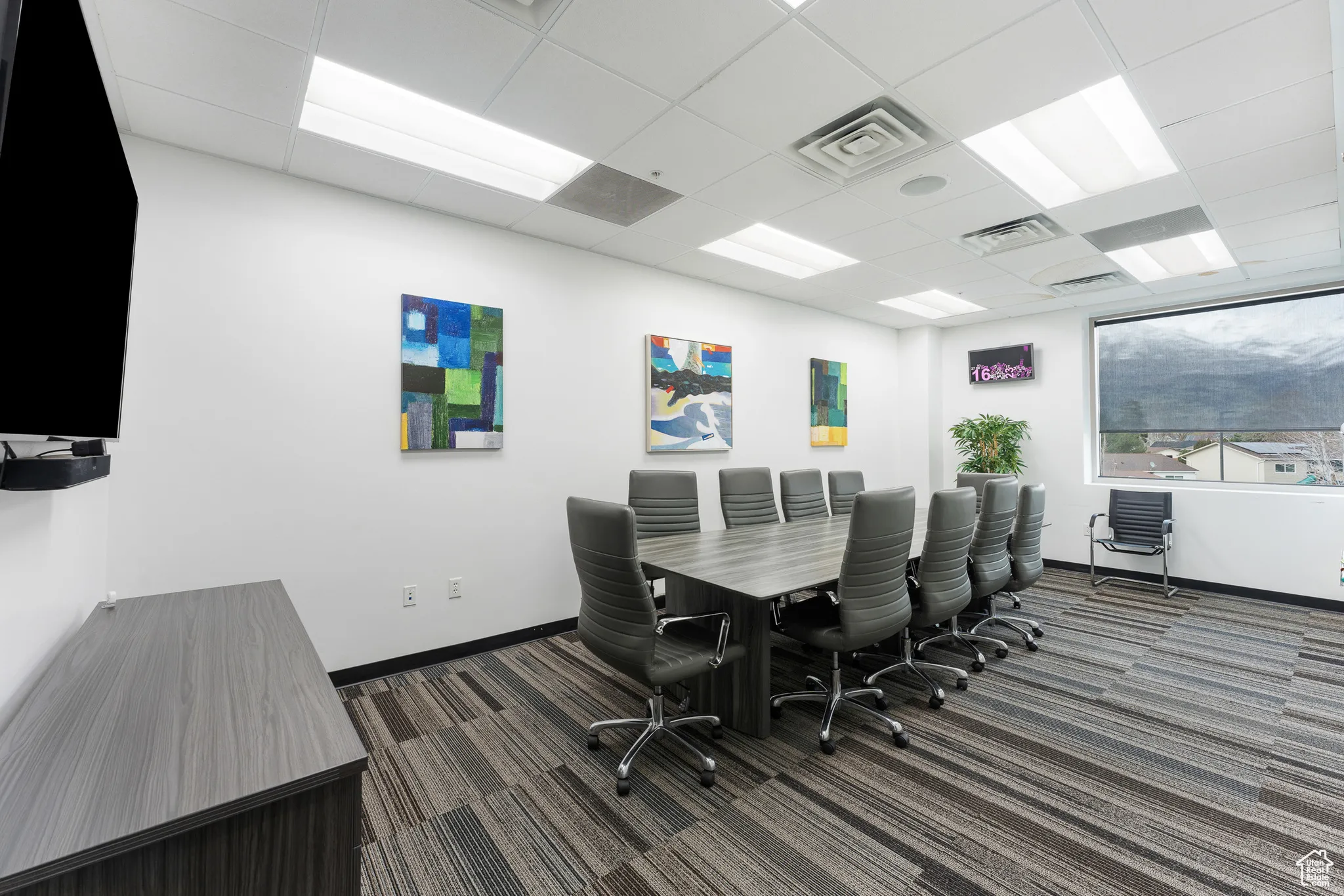 Carpeted office space with baseboards, visible vents, and a drop ceiling