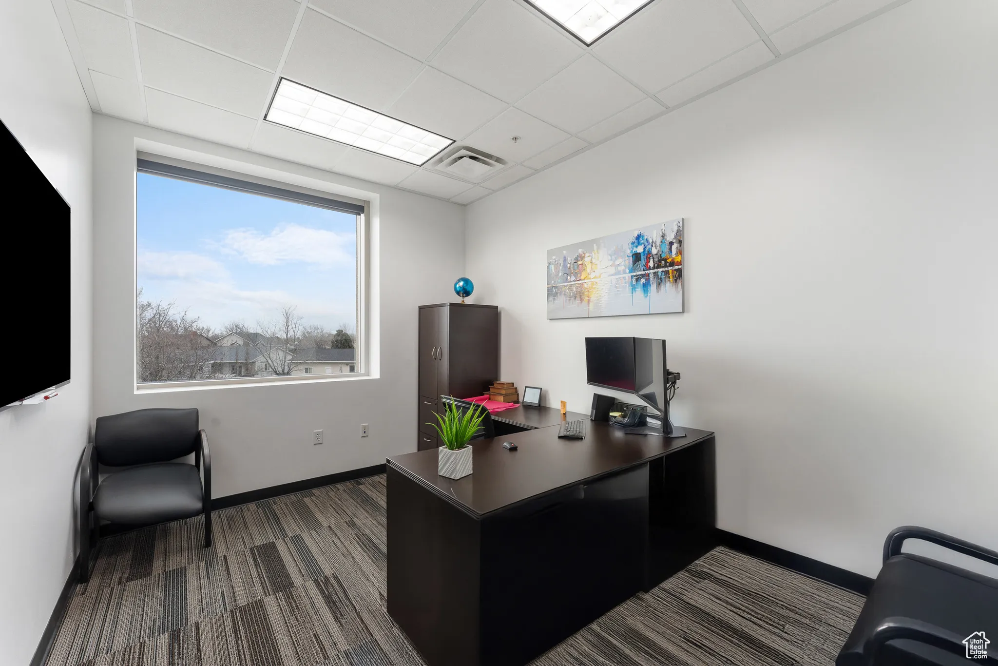 Office with a paneled ceiling, dark colored carpet, baseboards, and visible vents
