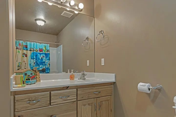 Bathroom vanity featuring a light-toned countertop, wood-finish cabinetry with silver-tone hardware, and a large wall-mounted mirror
