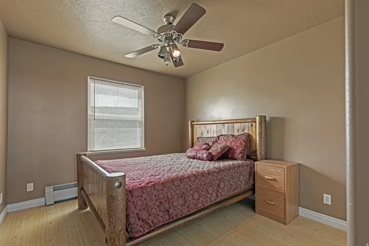 Bedroom featuring wood-finish flooring, a window with blinds, a ceiling fan with integrated lighting, and a baseboard heater