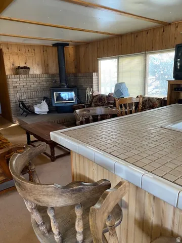 Kitchen featuring tile countertops, a wood stove, wooden walls, open floor plan, and a kitchen breakfast bar