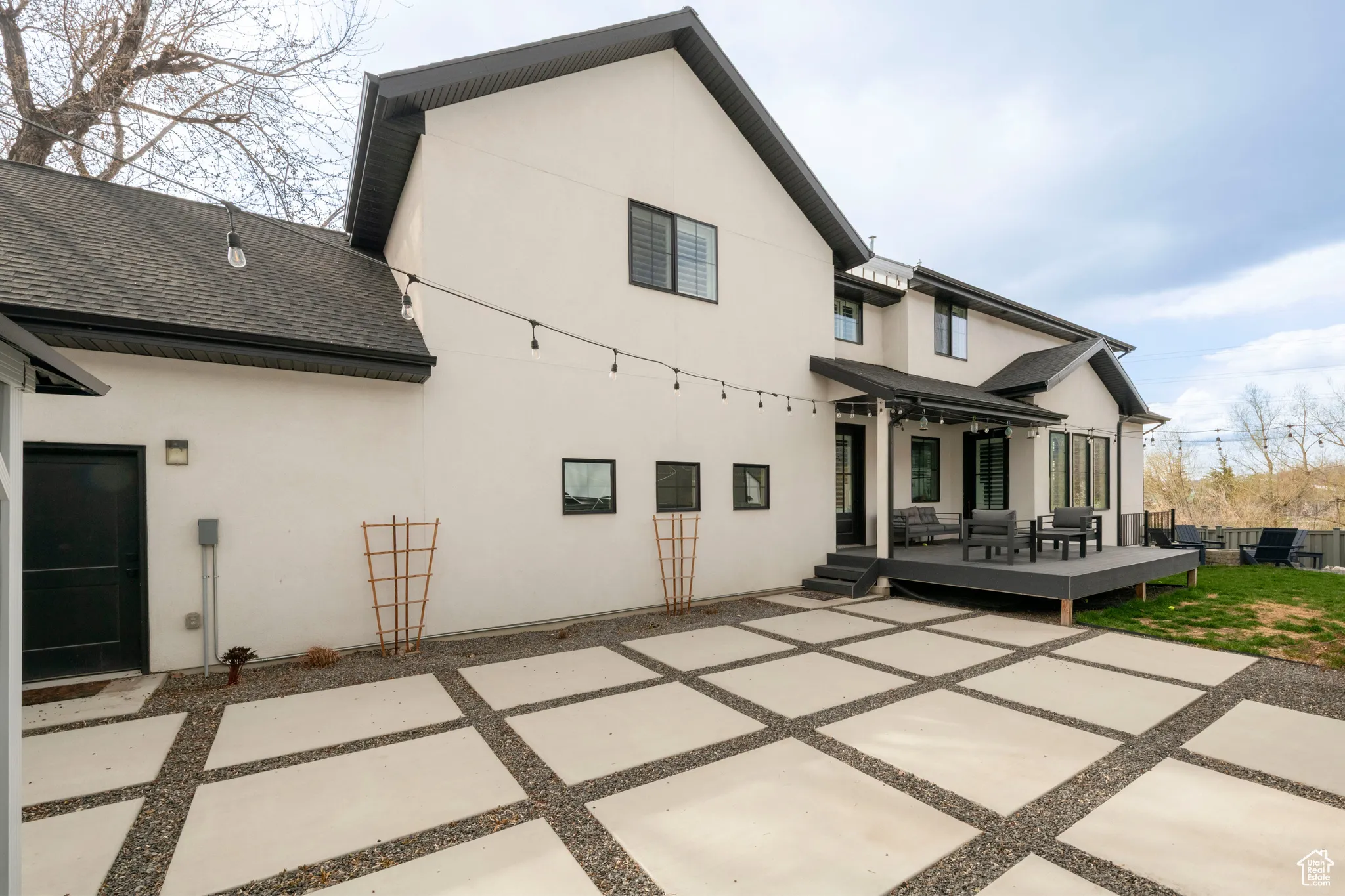 Rear view of house featuring stucco siding, a deck, a patio, and roof with shingles