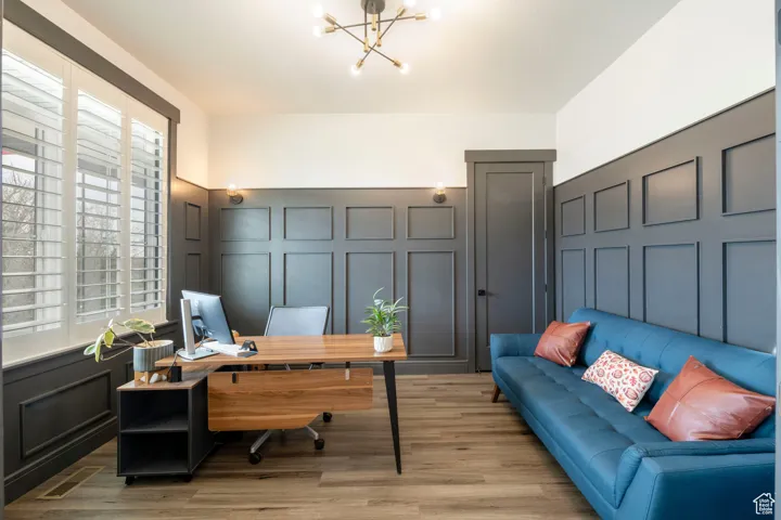 Home office featuring a decorative wall, a notable chandelier, light wood-style floors, and visible vents