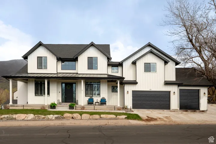 Modern farmhouse featuring covered porch, a standing seam roof, concrete driveway, an attached garage, and a shingled roof