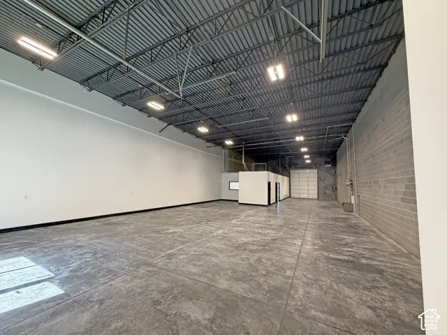 Expansive industrial space featuring a high exposed ceiling with metal trusswork, concrete flooring, and bright overhead lighting