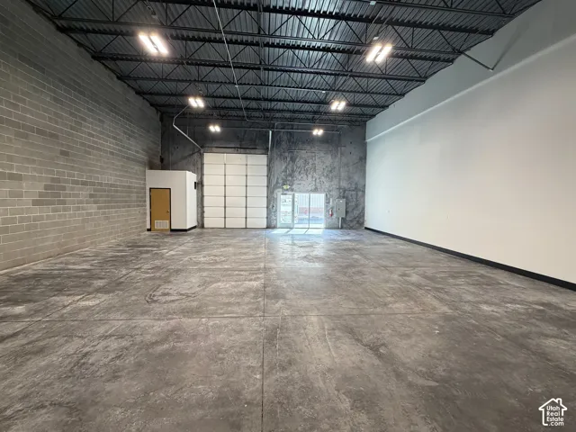 Spacious commercial interior featuring concrete flooring, exposed metal ceiling trusses, a large roll-up door, block wall construction, and recessed lighting fixtures
