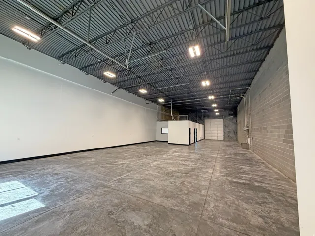 Expansive industrial space featuring a high exposed ceiling with metal trusswork, concrete flooring, and bright overhead lighting