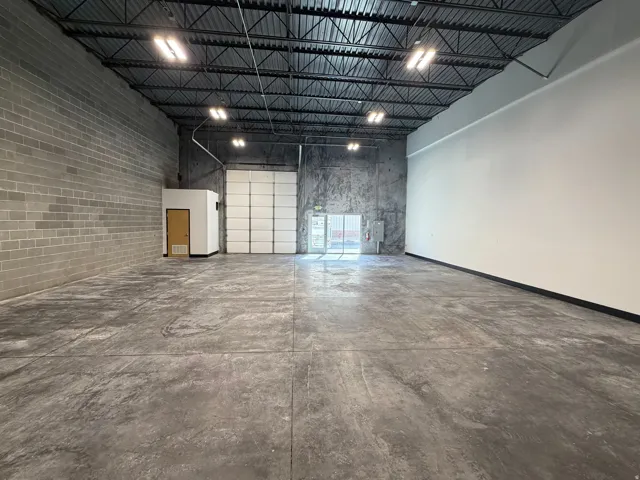 Spacious commercial interior featuring concrete flooring, exposed metal ceiling trusses, a large roll-up door, block wall construction, and recessed lighting fixtures