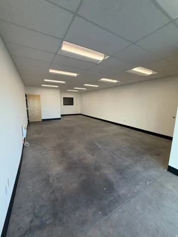 Expansive open-concept space featuring concrete flooring, a grid ceiling with integrated fluorescent lighting, and a neutral color palette