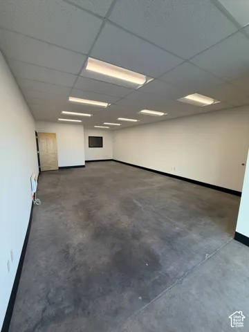 Expansive open-concept space featuring concrete flooring, a grid ceiling with integrated fluorescent lighting, and a neutral color palette
