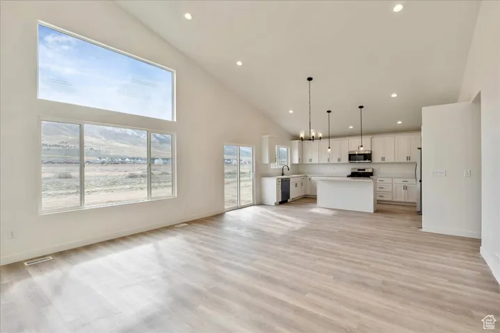 Kitchen with open floor plan, a kitchen island, appliances with stainless steel finishes, high vaulted ceiling, and light wood finished floors