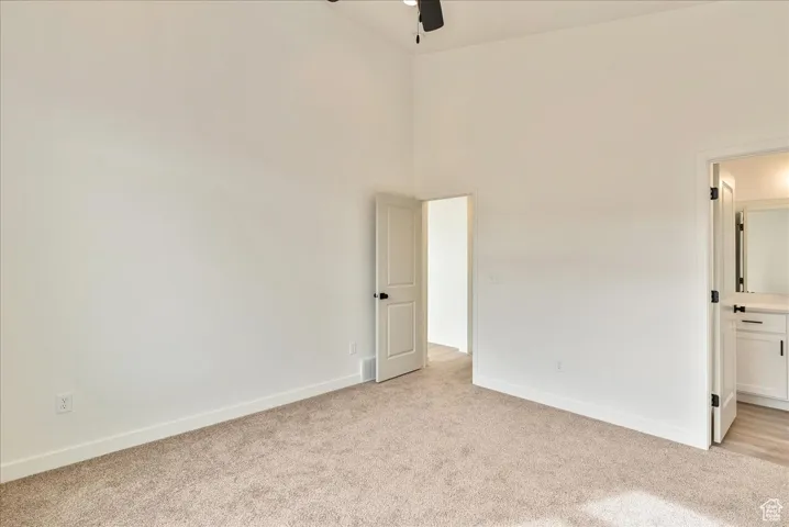 Spare room with light carpet, a high ceiling, ceiling fan, and baseboards