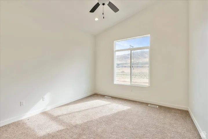 Spare room featuring baseboards, vaulted ceiling, light carpet, visible vents, and ceiling fan