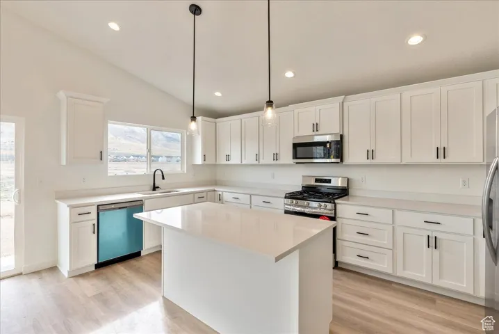 Kitchen featuring light countertops, white cabinets, appliances with stainless steel finishes, light wood finished floors, and a sink