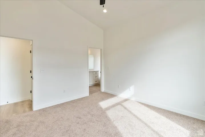 Unfurnished bedroom with baseboards, high vaulted ceiling, and light carpet