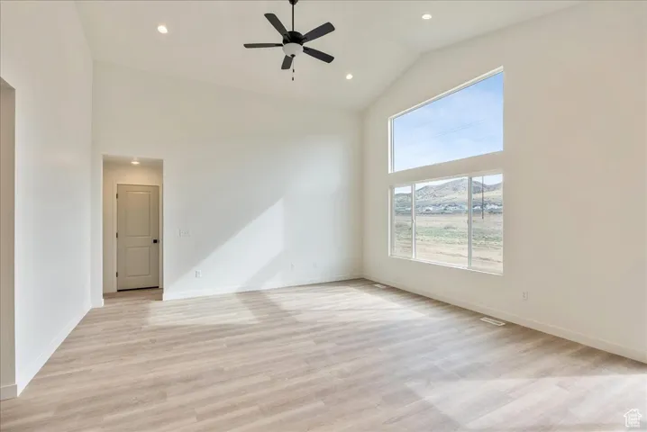Empty room featuring high vaulted ceiling, light wood-style floors, baseboards, and ceiling fan