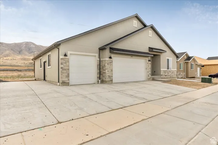View of front of house featuring stone siding, a garage, stucco siding, and concrete driveway