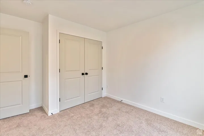 Unfurnished bedroom featuring light carpet, baseboards, and a closet