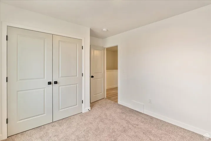 Unfurnished bedroom featuring a closet, light colored carpet, baseboards, and visible vents