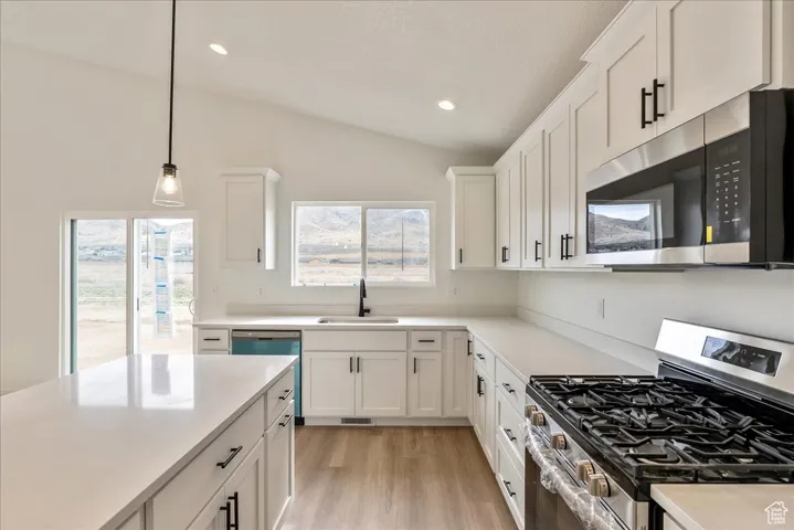 Kitchen featuring white cabinets, a sink, light countertops, stainless steel appliances, and lofted ceiling