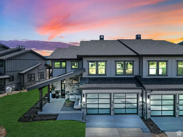 Back of property featuring stone siding, an attached garage, concrete driveway, board and batten siding, and roof with shingles