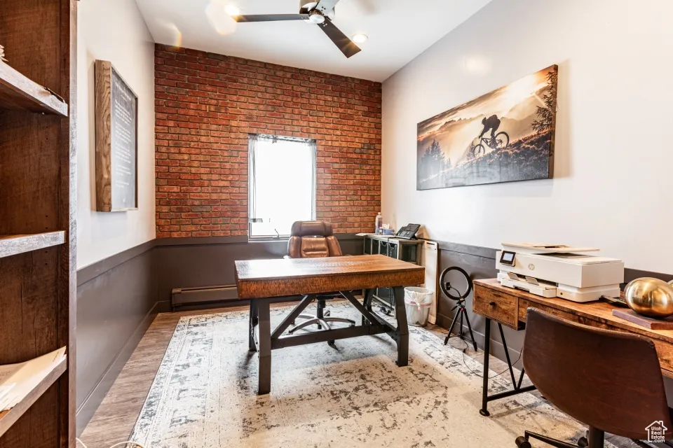 Office with light wood-style flooring, brick wall, ceiling fan, and wainscoting