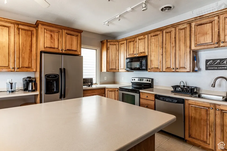 Kitchen featuring stainless steel appliances, brown cabinetry, a sink, and light tile patterned flooring