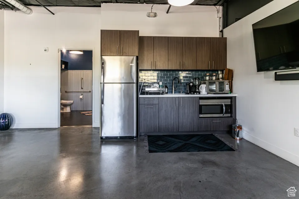 Kitchen featuring tasteful backsplash, finished concrete floors, a sink, light countertops, and stainless steel appliances