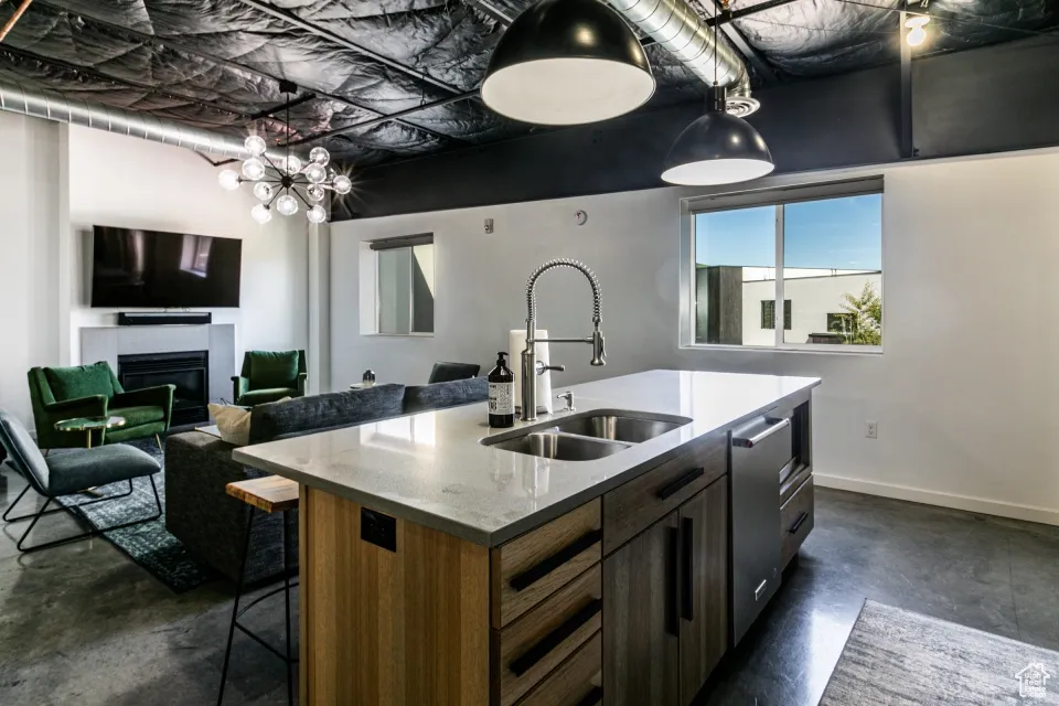 Kitchen featuring concrete floors, a glass covered fireplace, a kitchen island with sink, a sink, and baseboards