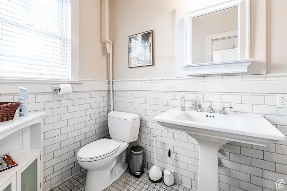Half bathroom featuring tile patterned flooring, wainscoting, tile walls, and toilet