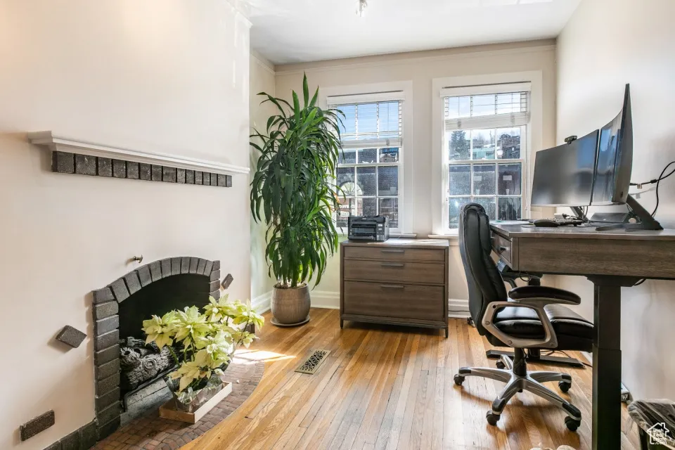 Home office with light wood finished floors, baseboards, visible vents, and a fireplace