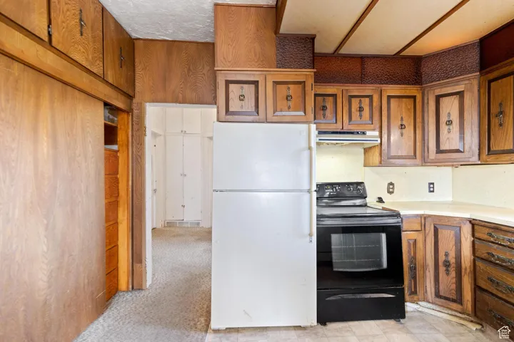 Kitchen featuring light countertops, freestanding refrigerator, brown cabinetry, under cabinet range hood, and black / electric stove