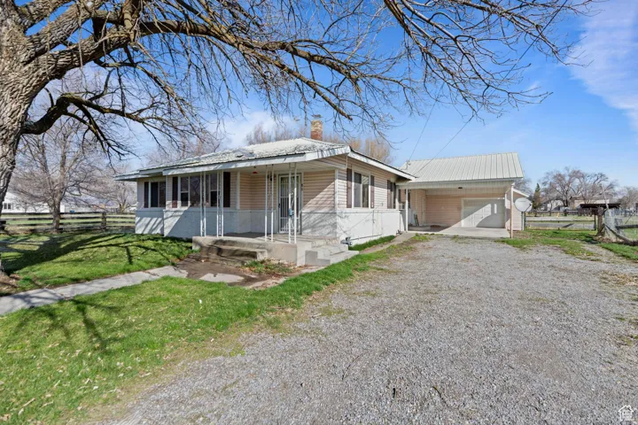 View of front of property with covered porch, gravel driveway, a front yard, and fence