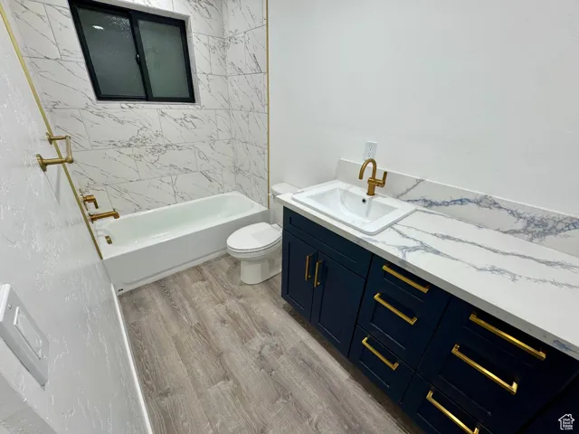 Bathroom featuring toilet, wood finished floors, vanity, and  shower combination