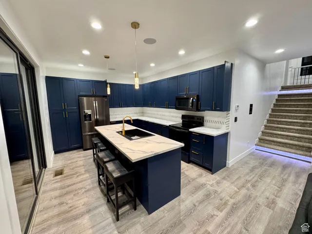Kitchen featuring a kitchen bar, light wood-type flooring, black appliances, blue cabinets, and a sink