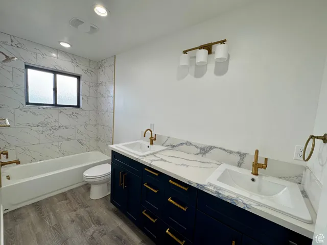 Full bath with toilet, wood finished floors, double vanity, and a sink