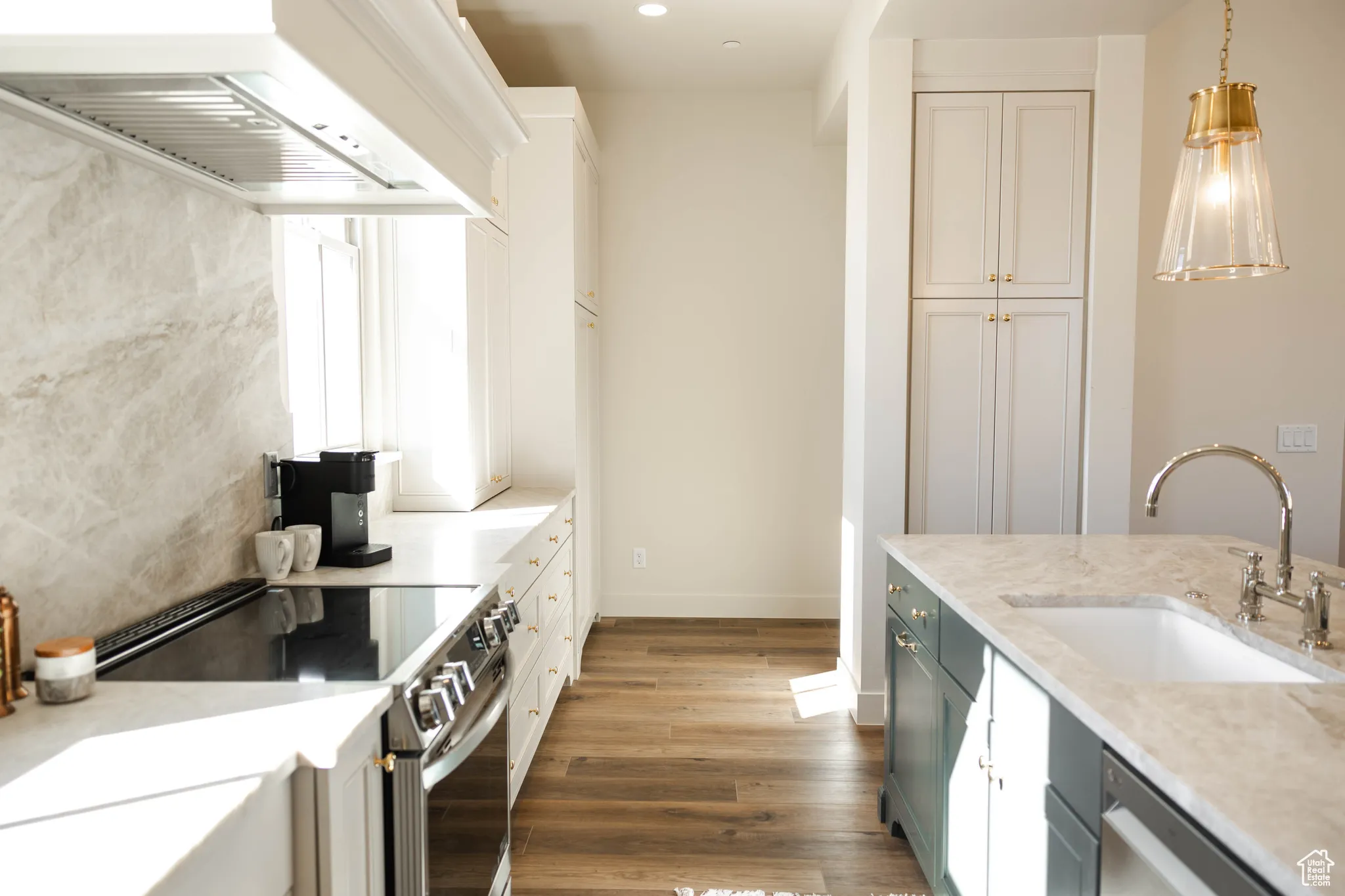 Kitchen featuring appliances with stainless steel finishes, wood finished floors, a sink, decorative light fixtures, and custom range hood