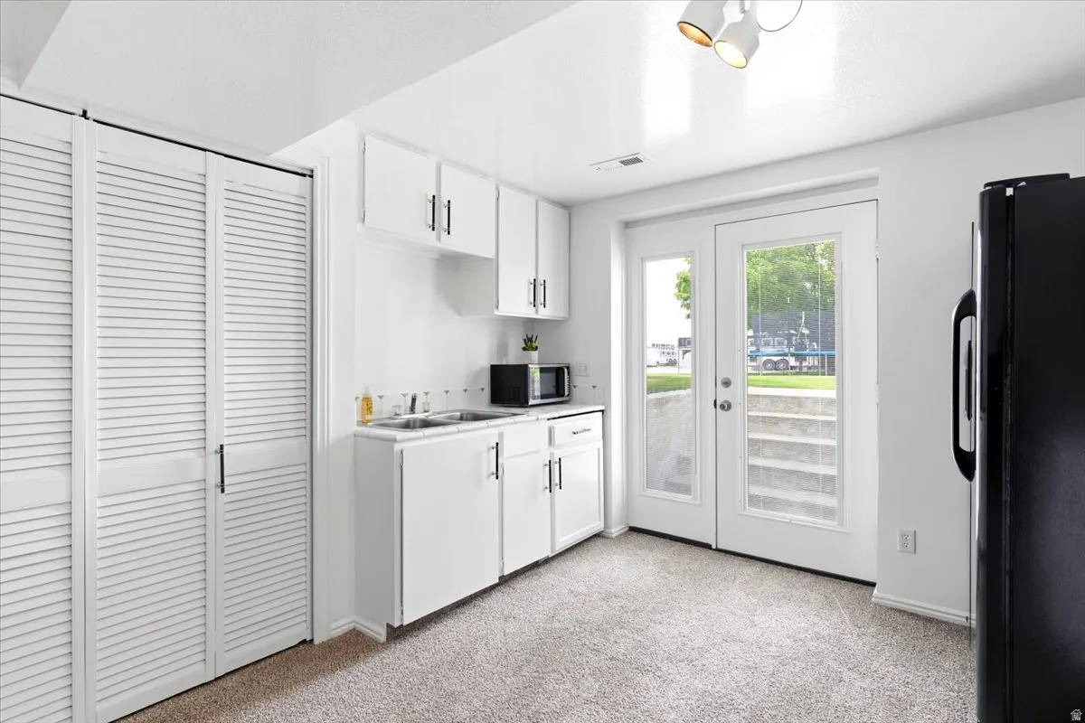 Compact kitchen space featuring white cabinetry, a double basin sink, and a black refrigerator
