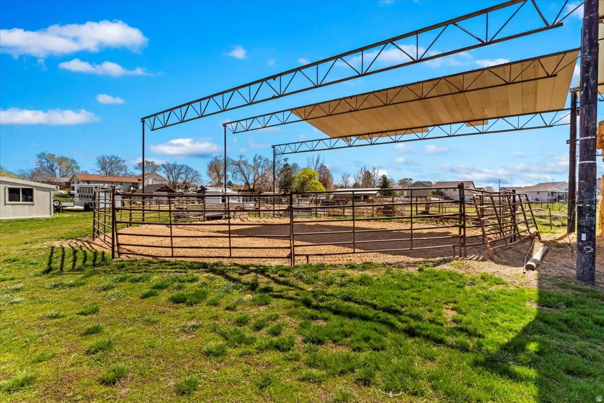 Outdoor arena with a metal frame shade structure, perimeter fencing, and a sand base
