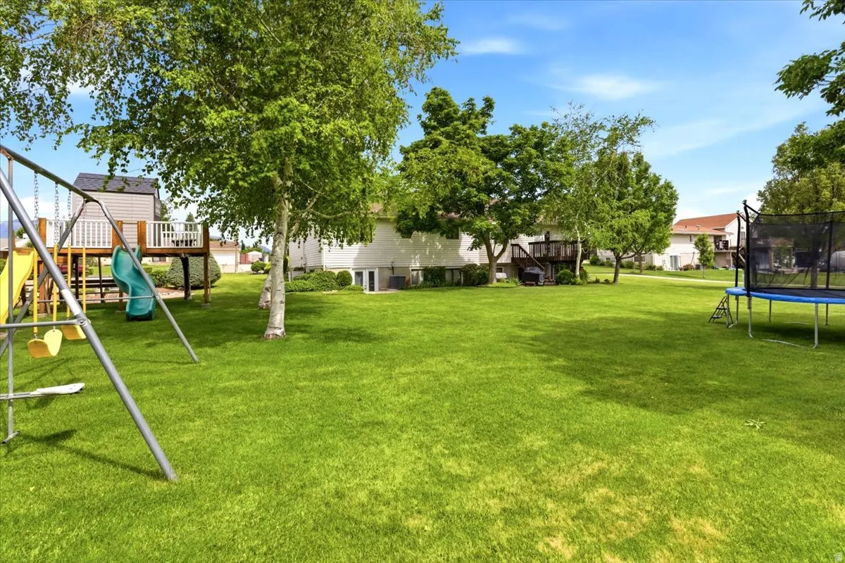 Spacious green lawn with mature trees, a multi-level deck, and a play structure featuring a slide