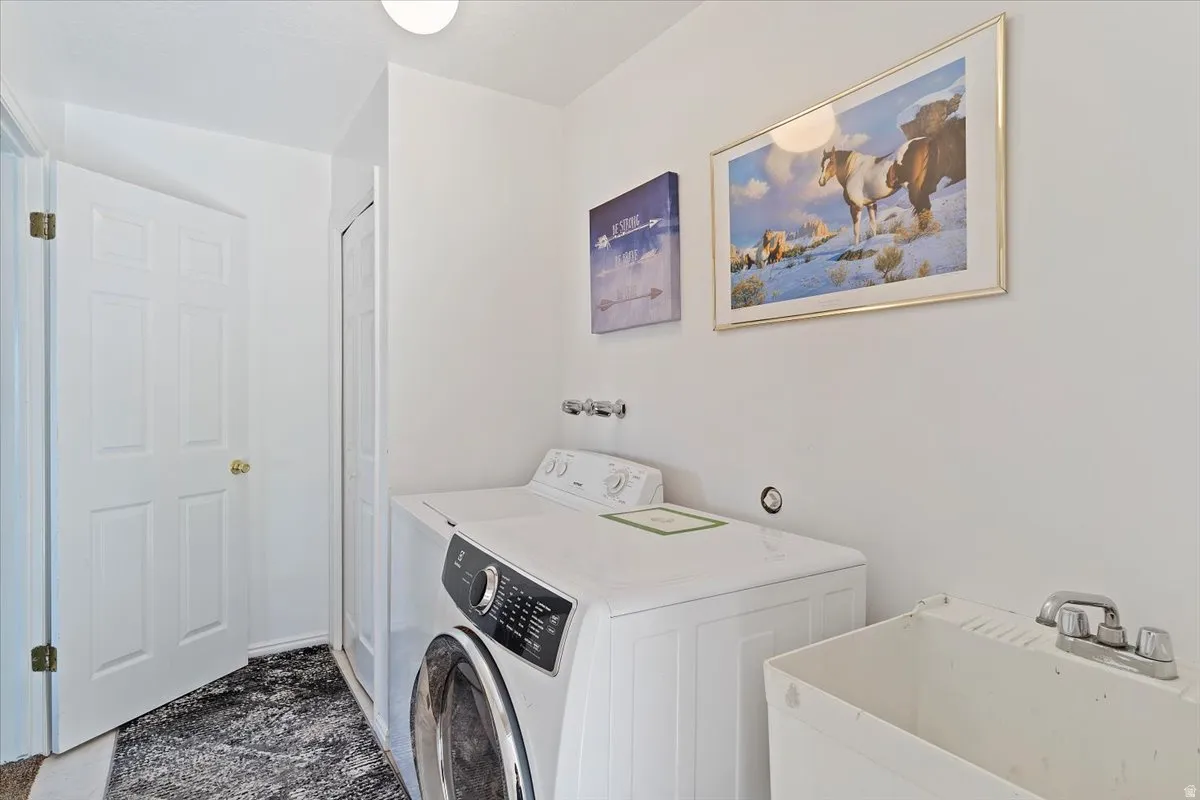 Dedicated laundry area featuring a front-load washing machine, a top-load washing machine, and a utility sink with a chrome faucet