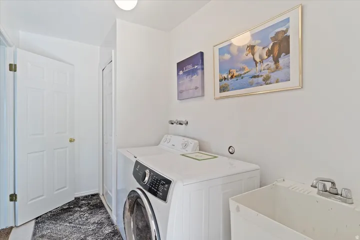 Dedicated laundry area featuring a front-load washing machine, a top-load washing machine, and a utility sink with a chrome faucet