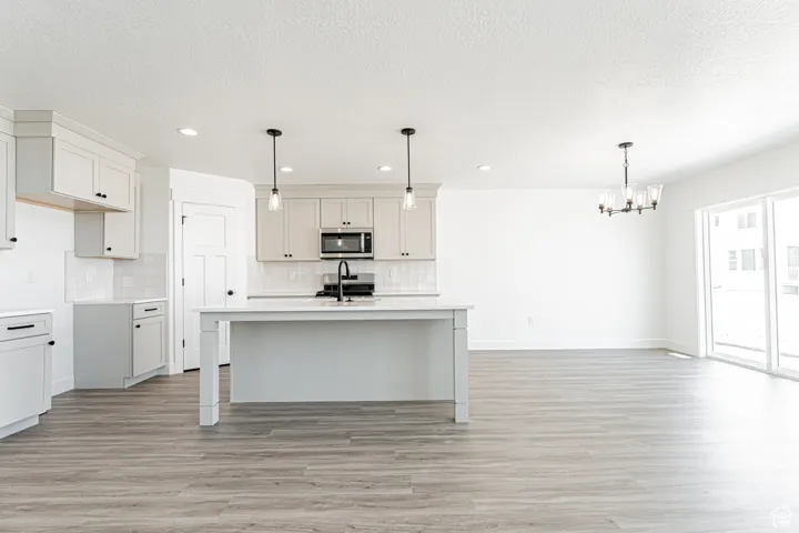 Kitchen with stainless steel microwave, a chandelier, backsplash, light wood-style flooring, and recessed lighting