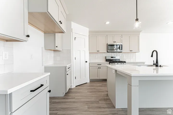 Kitchen featuring stainless steel appliances, tasteful backsplash, pendant lighting, recessed lighting, and light wood-type flooring