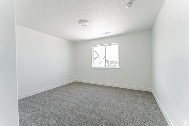Carpeted empty room with a textured ceiling and a smoke detector