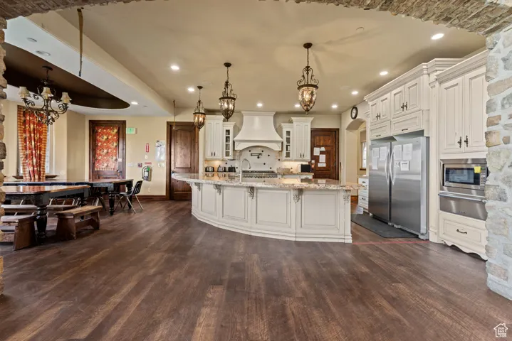 Kitchen with stainless steel appliances, custom exhaust hood, dark wood-type flooring, and an inviting chandelier