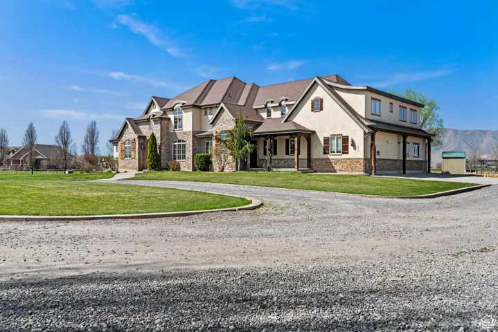View of front facade featuring curved driveway, stucco siding, stone siding, and a front yard