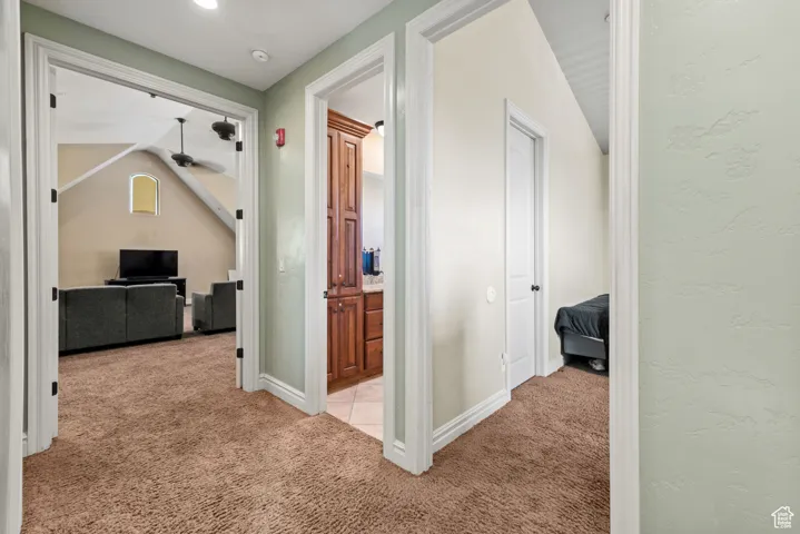 Hallway with baseboards, light colored carpet, and vaulted ceiling