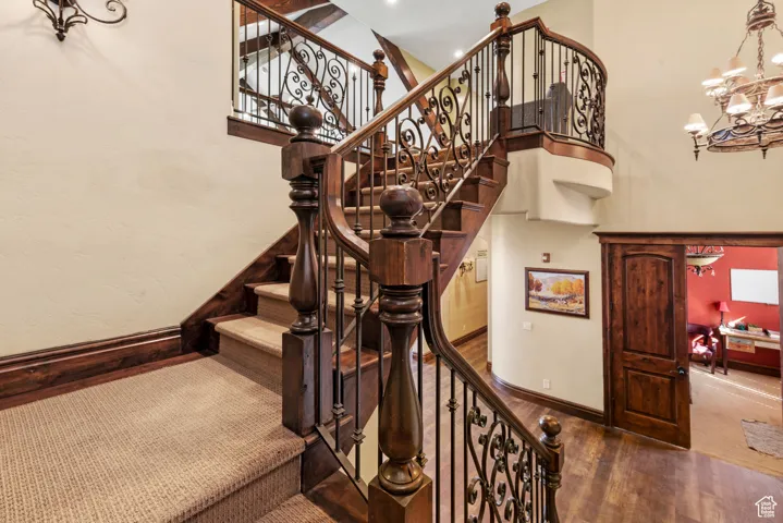 Stairs with wood finished floors, a notable chandelier, baseboards, and a towering ceiling