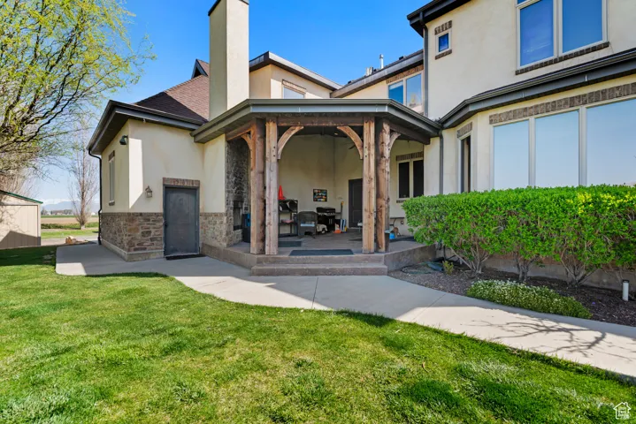 Rear view of house with a patio area, stucco siding, stone siding, and a lawn